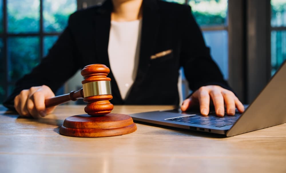 Female judge in a courtroom with the gavel, working with, computer and docking keyboard, eyeglasses, on table in morning light