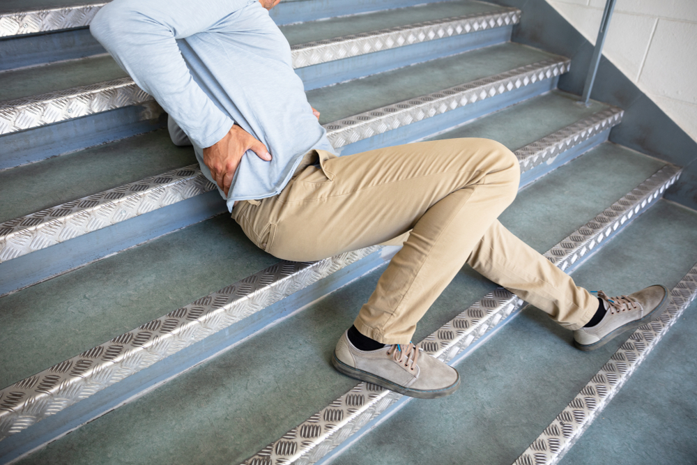 Man sitting on stairs holding his back after a fall, symbolizing injury from unsafe property conditions.