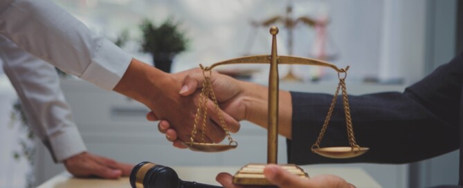 Lawyer and client shaking hands at desk with legal scales and gavel
