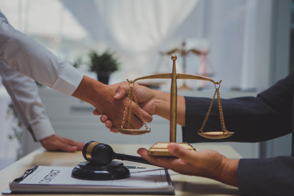Lawyer and client shaking hands at desk with legal scales and gavel
