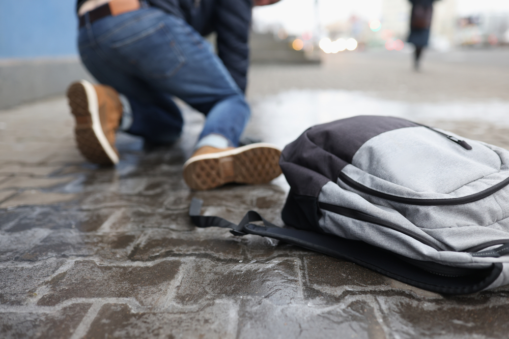 Person slipping on a wet sidewalk with a backpack nearby, representing a premises liability accident.