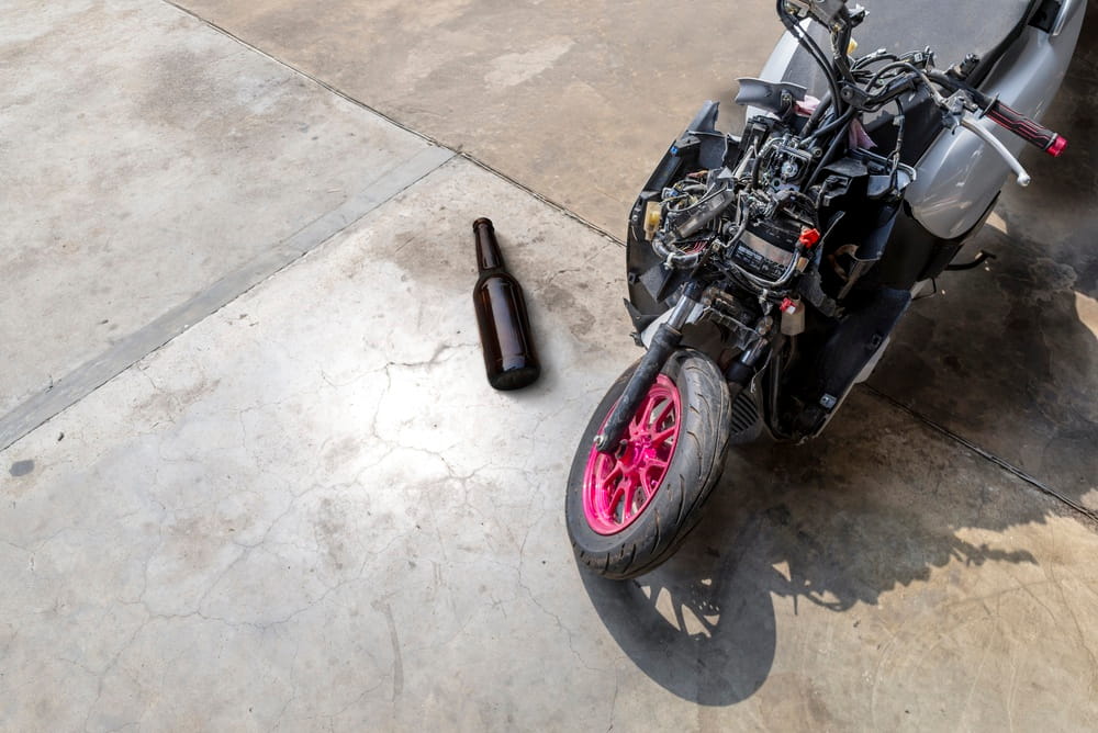 Damaged motorcycle near an alcohol bottle, representing a potential impaired driving crash.